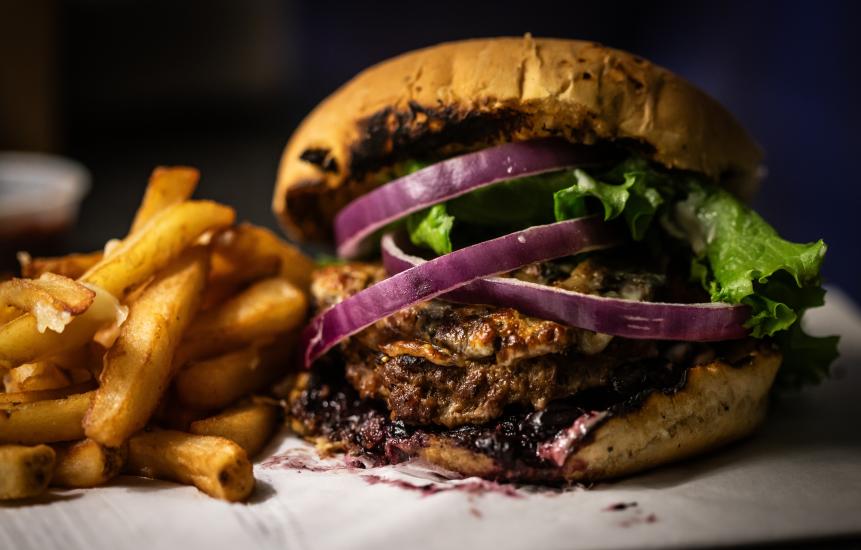 Close up of the Saskatoon berry bison burger with red onions, lettuce, and side fries.