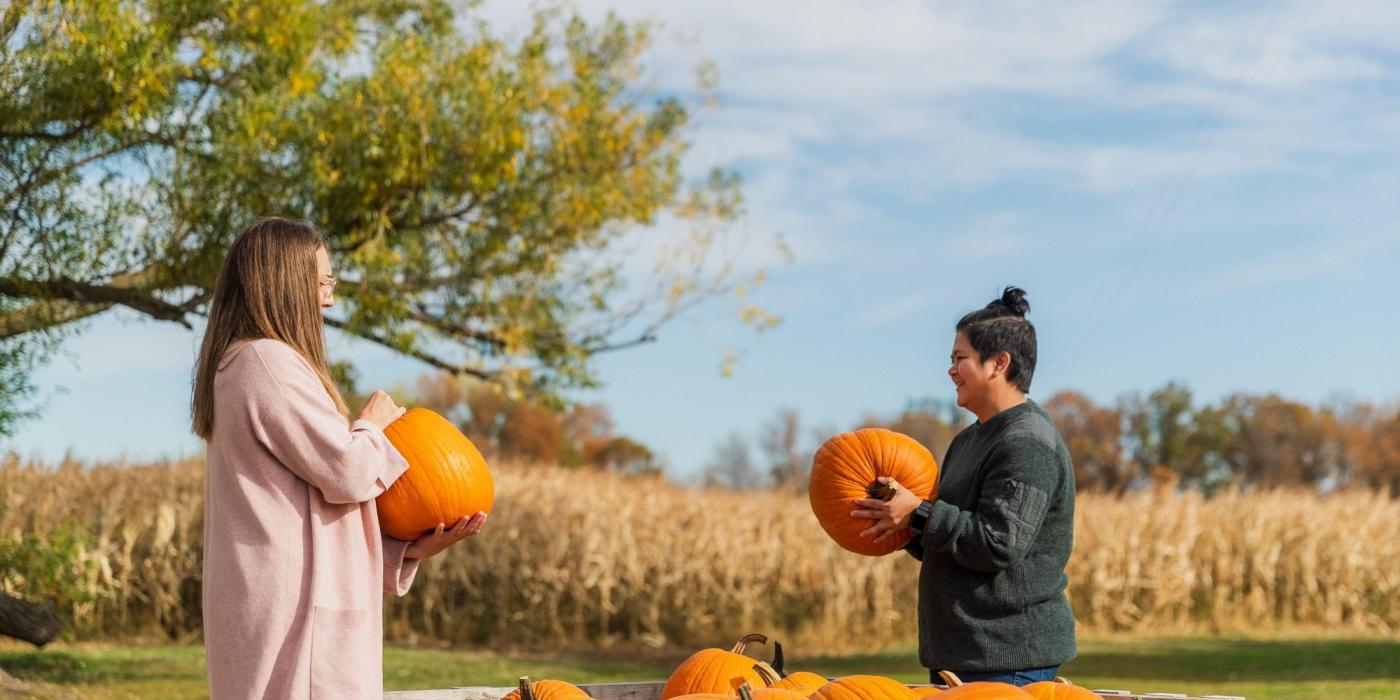 Two women each holding a medium-sized orange pumpkin at a pumpkin patch in Manitoba