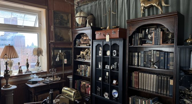 Un coin d'une boutique d'antiquités faiblement éclairée, avec des objets de collection en laiton et des bibliothèques en bois foncé remplies de livres anciens.