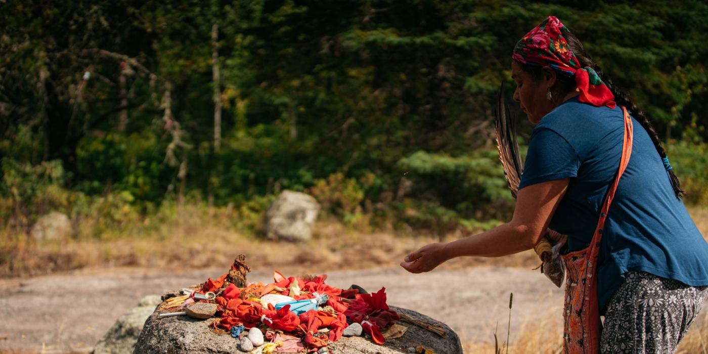 Una persona que realiza una bendición deposita una ofrenda sagrada sobre una roca.