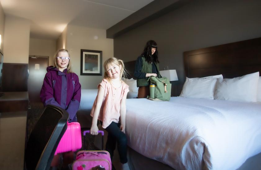 Interior of the hotel room while the two daughters pose with their suitcases.