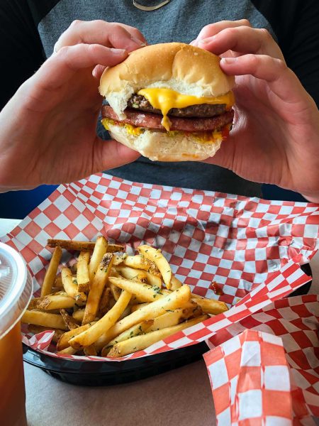 Two hands hold a burger over a basket of french fries