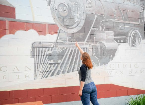 A person points upward at a mural of a train painted on the side of a building