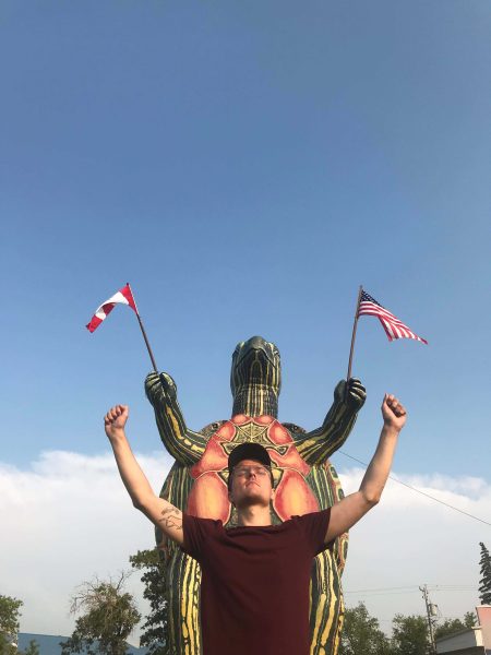 A person stands in front of the roadside attraction Tommy the Turtle, with both arms up, mimicking the stance of the statue