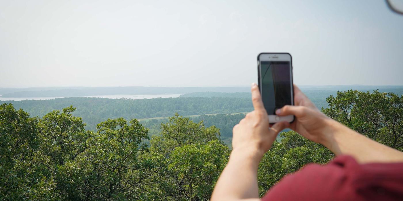 Person taking a photo with their phone of the view from the viewing tower of the Turtle's Back Trail.