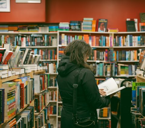 Woman is reading a book in the aisle of Whodunit? bookstore in Winnipeg, Manitoba.