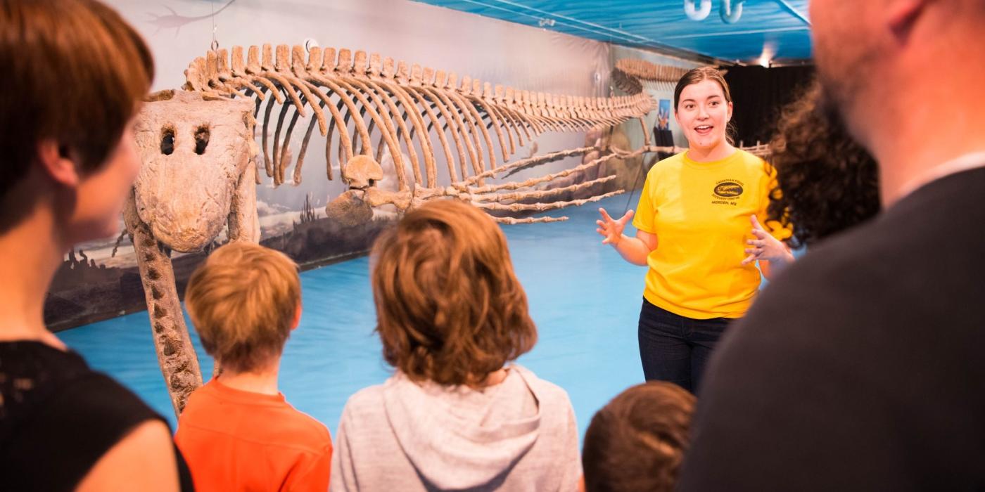 A tour group with kids and adults learning about mosasaurs and fossils from a tour guide.