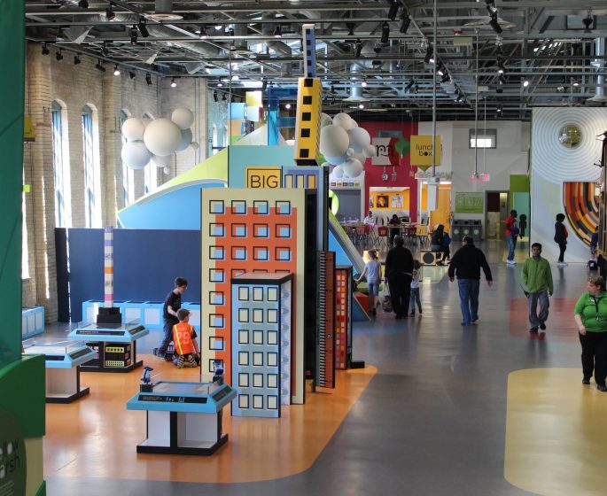 Inside a children's museum with colorful displays, kids playing, and people walking around.