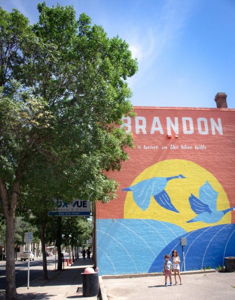 Zwei Kinder stehen vor einem Wandgemälde mit einem Sonnenuntergang und kanadischen Gänsen, das sich an der Seite eines Gebäudes in der Innenstadt von Brandon befindet.