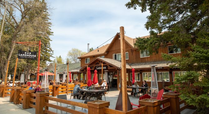 Gente sentada en mesas bajo sombrillas, rodeada de árboles, en el patio del restaurante Lakehouse.