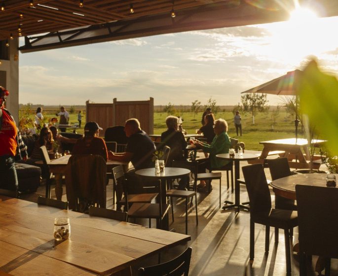 Cozy cidery taproom with open-air seating, bathed in warm sunlight and overlooking scenic prairie views.