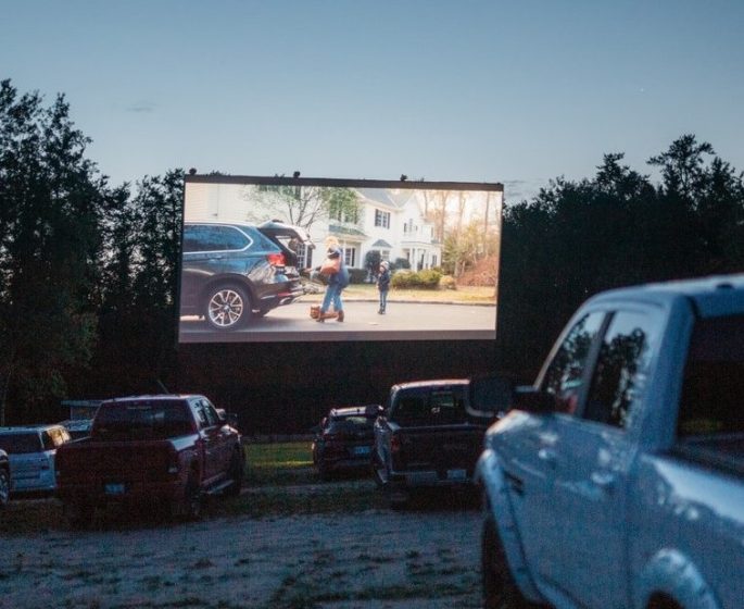 Nakapila ang mga sasakyan na nanonood ng malaking screen ng pelikula sa isang drive-in movie theater