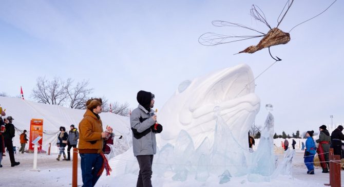 Des visiteurs admirant une sculpture de neige et dégustant de la tire d'érable au Festival du Voyageur