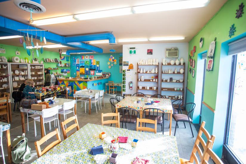 Interior of a brightly coloured pottery studio lined with wooden shelves and tables with space to paint and create.