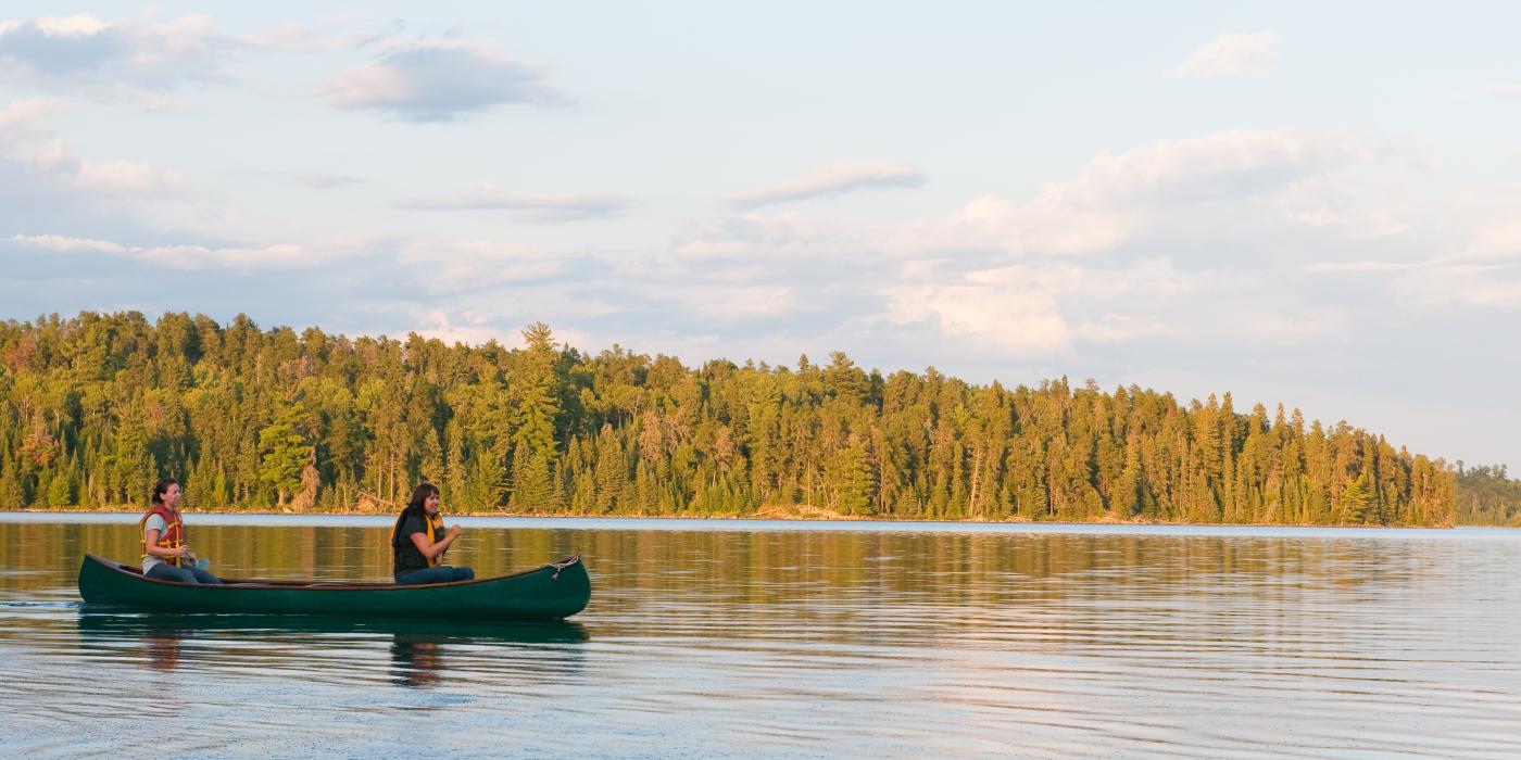 Two women in a green canoe on a lake with forest in the background