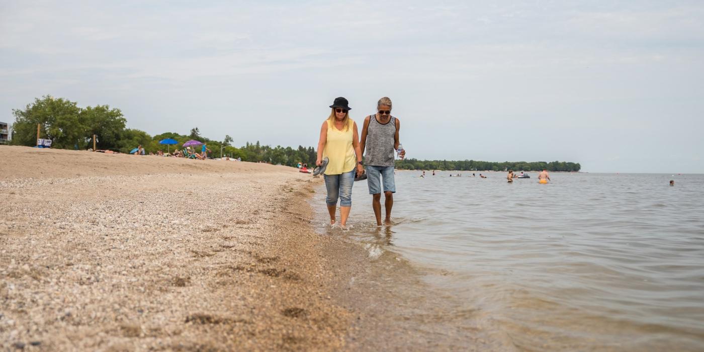Zwei Personen, die am Strand von Gimli am Wasser entlang spazieren.