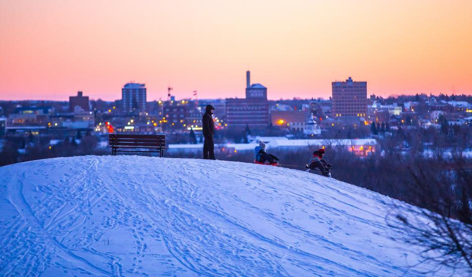 View of the top of Hanbury Hill with sledders going down and a sunset in the background.