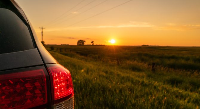 Looking past the tail lights on a car at the sunset over a farm field.