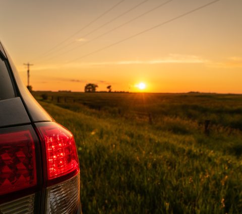 En regardant au-delà des feux arrière d'une voiture, on voit le coucher de soleil sur un champ de ferme.