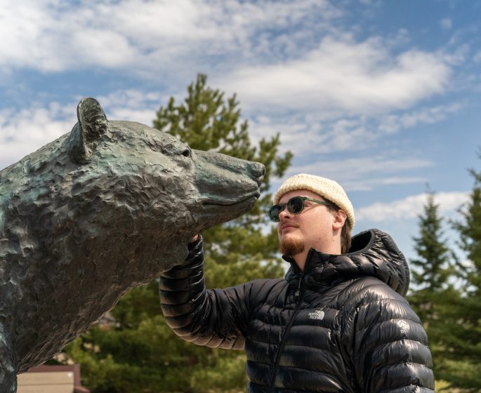 Man touching the bronze bear statue at the Peter Sawatzky Sculpture Park on a sunny day.