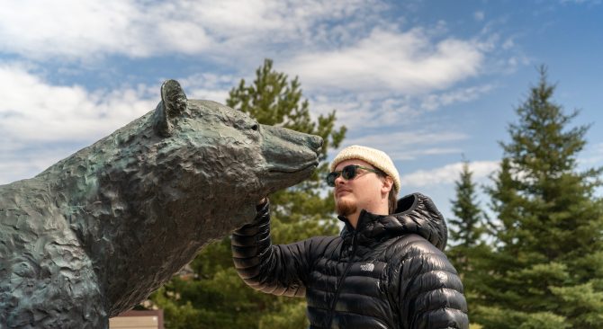 Man touching the bronze bear statue at the Peter Sawatzky Sculpture Park on a sunny day.
