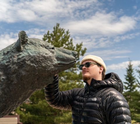 Man touching the bronze bear statue at the Peter Sawatzky Sculpture Park on a sunny day.