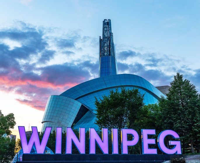 Schild von Winnipeg vor dem Kanadischen Museum für Menschenrechte bei Sonnenuntergang