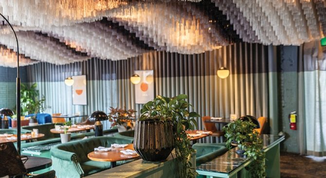 Intérieur de restaurant élégant, avec des sièges verts, des plantes décoratives et un plafond au design unique orné d'éléments suspendus.