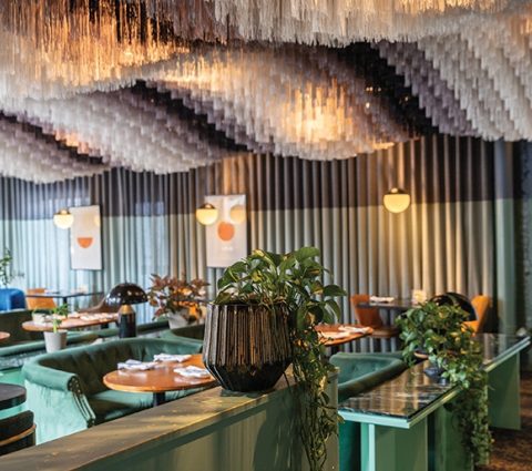 Stylish restaurant interior featuring green seating, decorative plants, and a unique ceiling design with hanging elements.