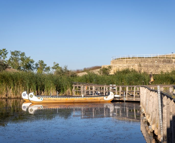 Un lac avec deux canoës traditionnels près d'une passerelle menant au bâtiment d'Oak Hammock Marsh à l'heure dorée.