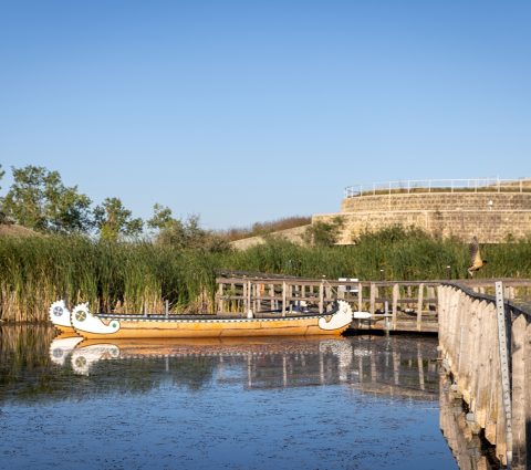 Un lac avec deux canoës traditionnels près d'une passerelle menant au bâtiment d'Oak Hammock Marsh à l'heure dorée.