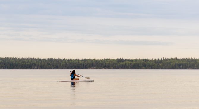 Woman sits down and paddleboards across a lake