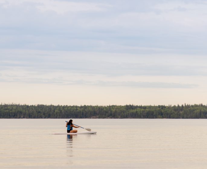 Woman sits down and paddleboards across a lake
