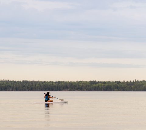 Woman sits down and paddleboards across a lake