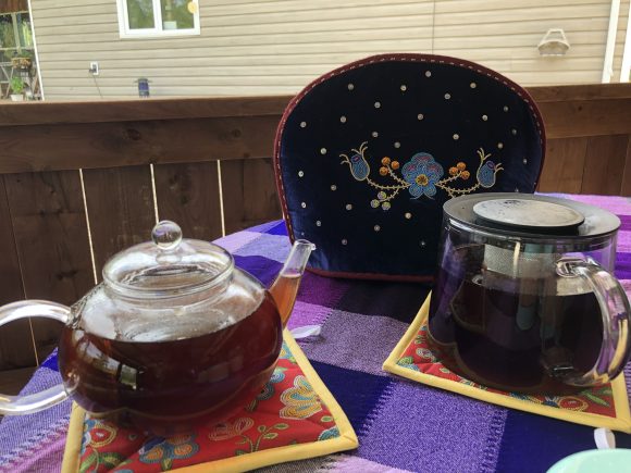 Zwei gläserne Teekannen stehen auf einem Tisch vor einem perlenbesetzten Teewärmer