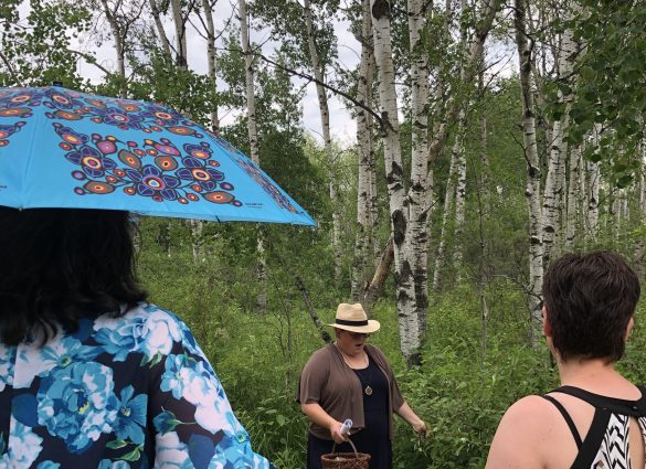 Zwei Personen stehen mit dem Rücken zur Kamera und beobachten eine dritte Person vor ihnen, die gerade einen Satz spricht.