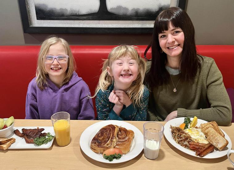 Mother and two daughters sit in a red booth with three breakfast plates in front of them.