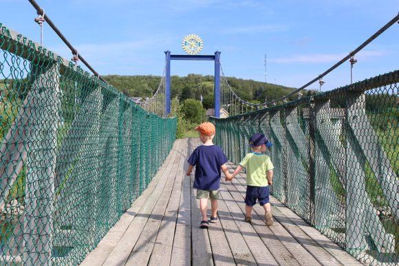 Zwei Kinder überqueren händchenhaltend eine Hängebrücke in Minnedosa