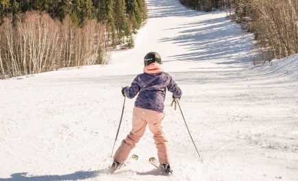 A young person, facing away from the camera, skis downhill at Mystery Mountain Winter Park in Thompson.