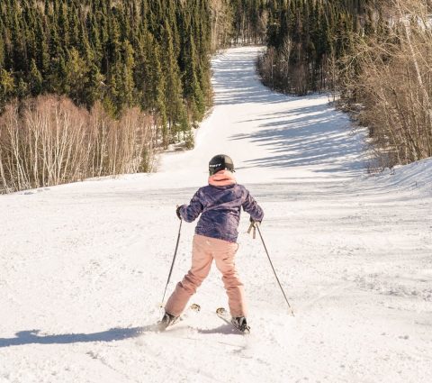 Isang kabataan, na nakatalikod sa camera, ang nag-ski pababa sa Mystery Mountain Winter Park sa Thompson.