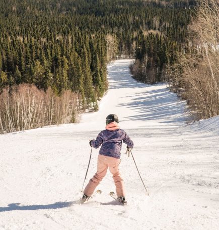 A young person, facing away from the camera, skis downhill at Mystery Mountain Winter Park in Thompson.