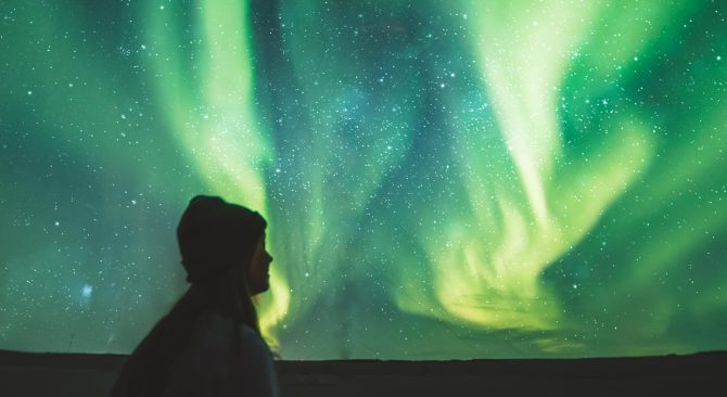 Silhouette ng isang taong nanonood sa mga berdeng ilaw ng hilagang ilaw na sumasayaw sa kalangitan.