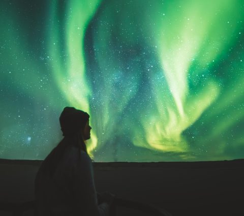 Silhouette einer Person, die das grüne Licht der Nordlichter am Himmel beobachtet.