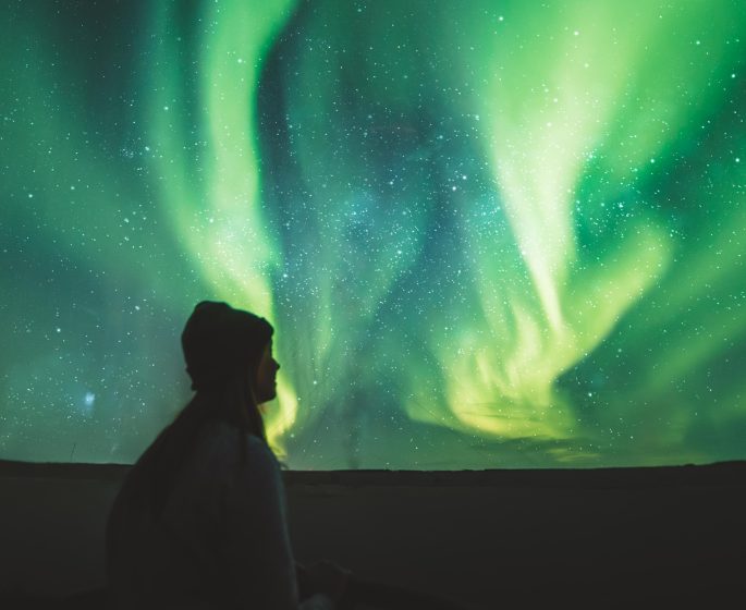 Silueta de una persona observando las luces verdes de la aurora boreal bailando en el cielo.