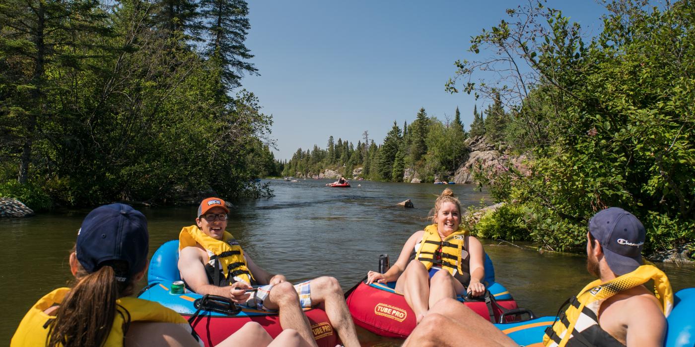 A group of people sitting in inner tubes floating down the Pinawa Channel on a sunny day.