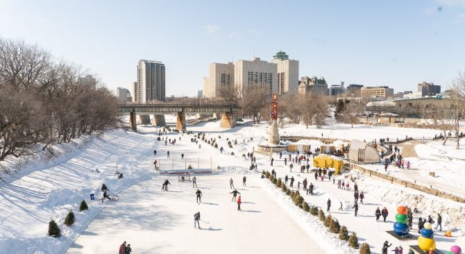 Vue du sentier mutuel de la rivière Rouge depuis le haut avec des personnes patinant sur la glace et des bâtiments en arrière-plan.