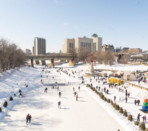 Vue du sentier mutuel de la rivière Rouge depuis le haut avec des personnes patinant sur la glace et des bâtiments en arrière-plan.
