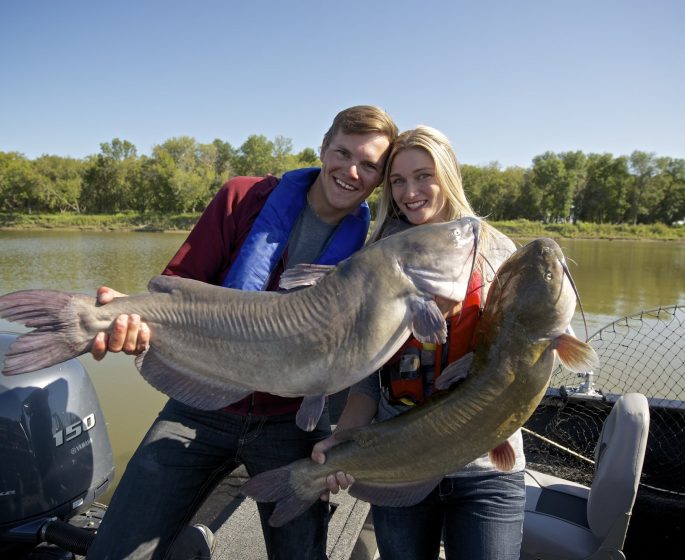 Dos personas, en una embarcación, sostienen un par de siluros de canal muy grandes capturados cerca de Selkirk.