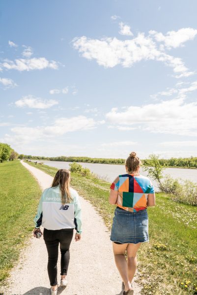 Dos personas caminan por un sendero del parque Selkirk a orillas del río Rojo en un día soleado.
