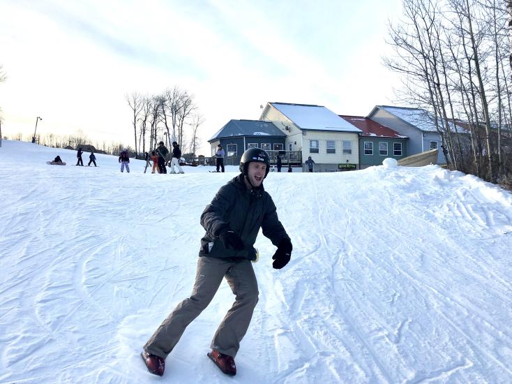 Man with a smile going down a ski hill with boots on his feet that look like ski boots.